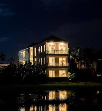 A three-story house at night in Hoi An, with lights on, reflecting in a calm body of water in front.