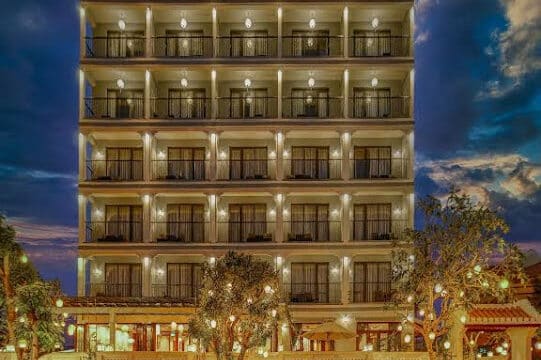 A brightly lit multi-story hotel building at dusk in Hoi An, with balconies and trees in front.