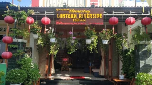Entrance of Lantern Riverside Homestay in Hoi An, decorated with red lanterns and lush green plants.
