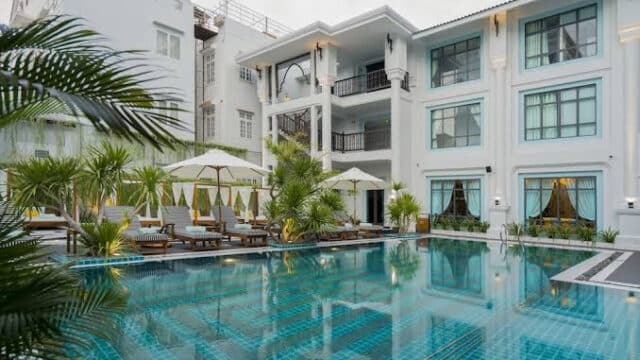 Modern Hoi An hotel with a large outdoor pool, lounge chairs, umbrellas, and lush tropical plants surrounding the water.