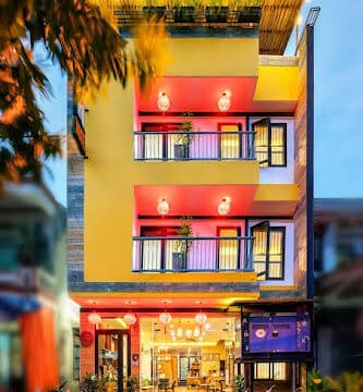 Three-story yellow Hoi An building with balconies, lantern lights, and bikes parked in front at dusk.