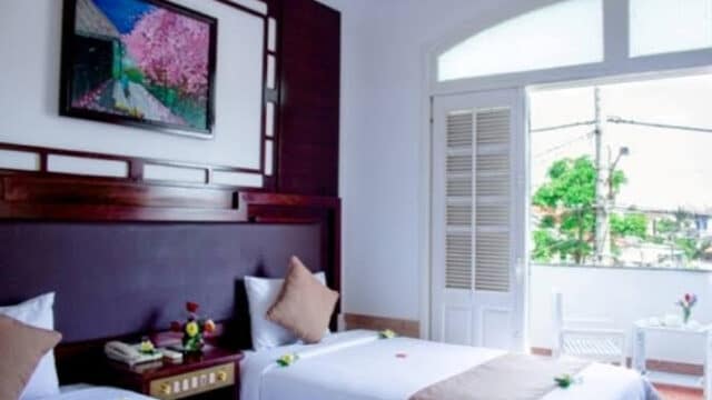 Bright Hoi An hotel room with two single beds, artwork above the headboard, and a door opening to a balcony.