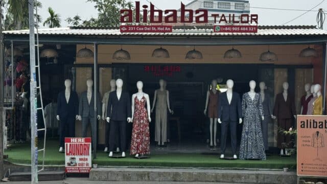 Storefront of Alibaba Tailor in Hoi An with mannequins in suits and dresses displayed outside.