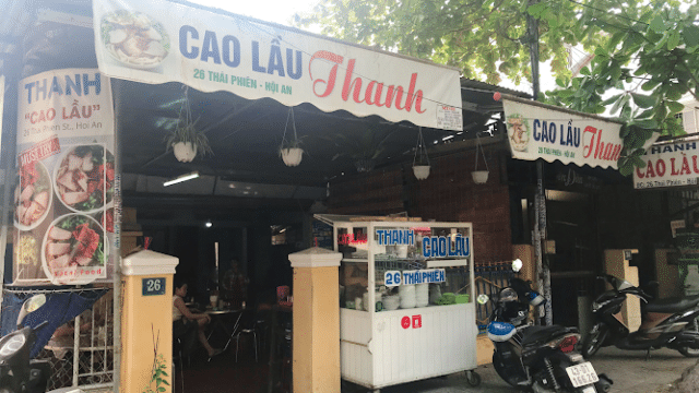 Street view of Thanh Cao Lầu restaurant in Hoi An, featuring a food cart and motorbikes parked outside.