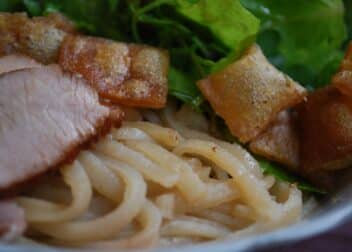 Close-up of a bowl of cao lau with noodles, pork, herbs and croutons