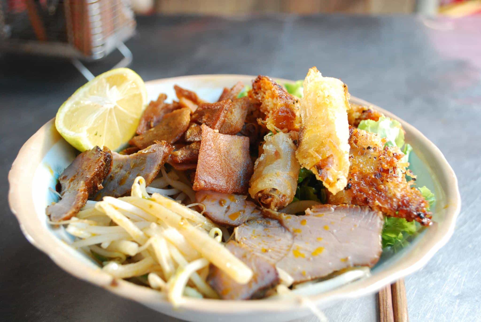 A bowl of cao lau served with spring rolls
