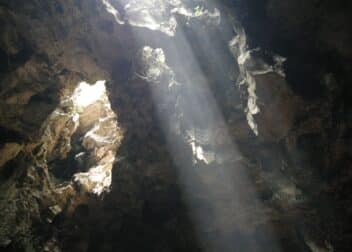 Sunlight streaming through the roof of Huyen Khong cave onto Buddhist statues, Marble Mountains