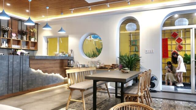 Modern, cozy cafe interior with wooden furniture; people entering through a door adorned with Hoi An-inspired red decorations.