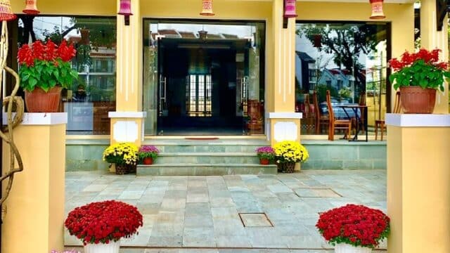 Entrance of Man Riverside Hotel adorned with potted red and yellow flowers and a sign above the doorway.