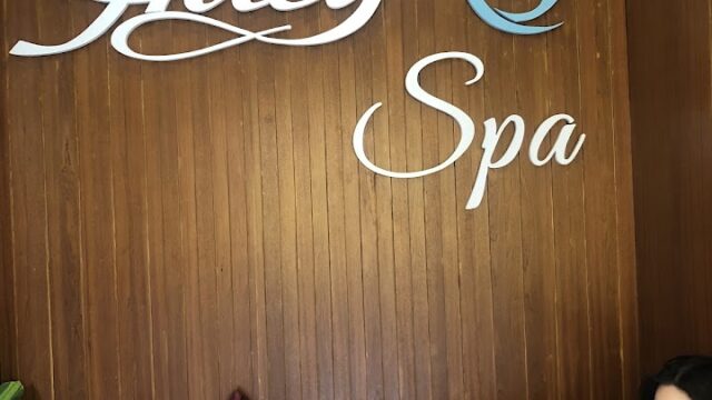 Wooden wall with Alley Spa sign, two cushions, a bag, and a woman sitting and looking at her phone.