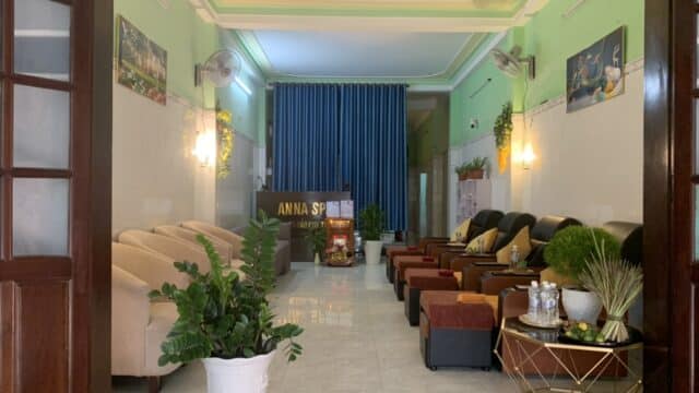 A cozy spa lounge with armchairs, potted plants, a reception desk, and soft lighting.
