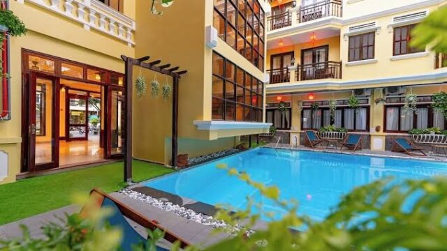Modern Annam Heritage boutique hotel courtyard with a clear blue swimming pool, glass doors, balconies with plants, and a serene spa.