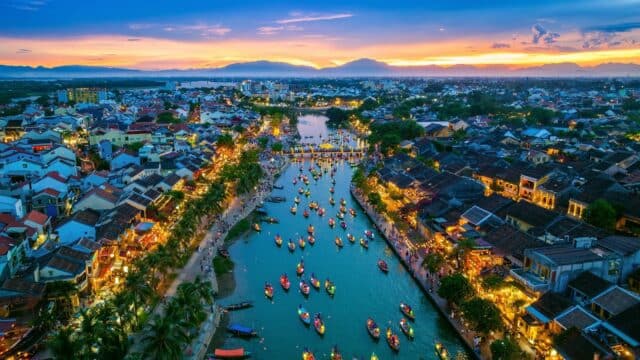 Aerial view of a river with colorful boats and city lights at sunset, perfect for Authentic Adventures amid vibrant city life.
