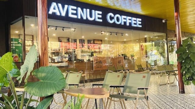 Outdoor seating area at Avenue Coffee in Hoi An, with green chairs, plants, and a bright yellow ceiling.