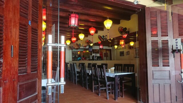 Cozy restaurant interior at Baba's Kitchen with wooden tables, chairs, and colorful lanterns hanging from the ceiling.
