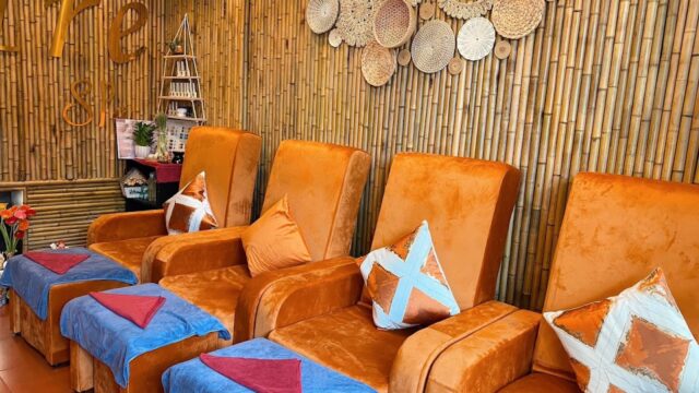 Four orange spa chairs with colorful pillows and blue towels in a room with bamboo walls and woven decor.