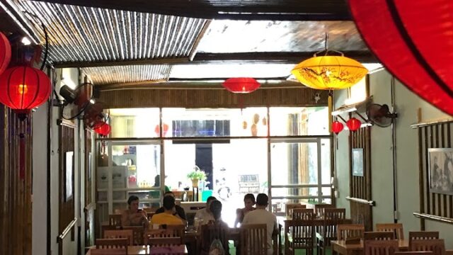 Dimly lit Bamboo Restaurant with wooden tables, red lanterns, and a few people seated at the back near the windows.