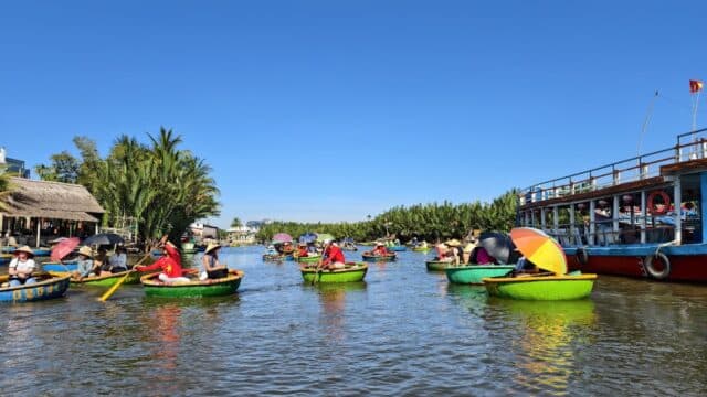 People riding round bamboo basket boats on a river during a Bay Mau Coconut Forest tour, with trees and boats in the background.