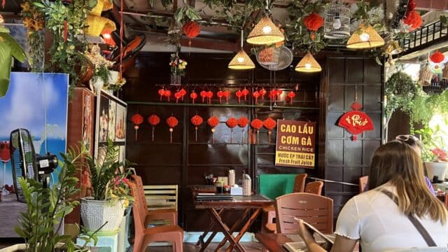 Vietnamese restaurant interior with lanterns, hanging plants, and a woman reading a menu at a table.