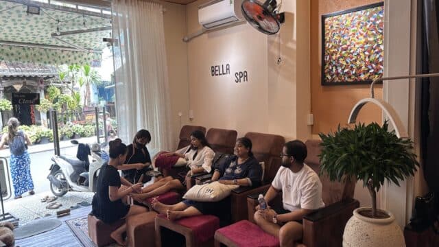 People relaxing and getting foot massages inside Bella Spa, a welcoming nail salon with a street view visible through the open entrance.