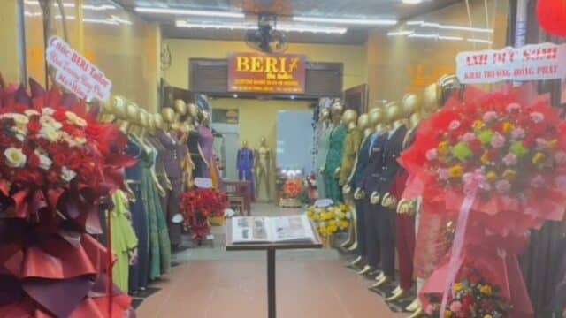 A tailor shop entrance in Hoi An with flower stands, mannequins in suits, and a sign reading BERLY the tailor.