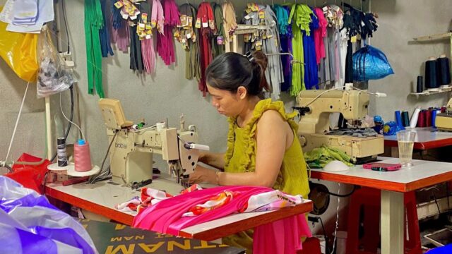 A woman in a yellow top sews colorful fabric at a sewing machine in a vibrant Hoi An workshop.