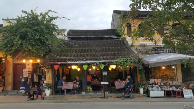 Street cafe with lanterns, people dining outside, and market stalls in front of the rustic Blue Dragon Restaurant.