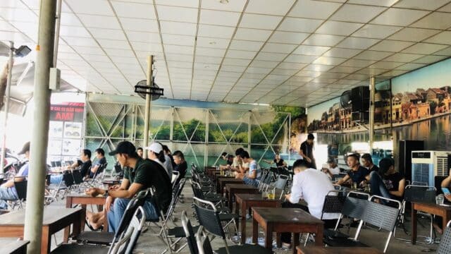 People sitting at tables in a bright, spacious café in Hoi An, with wall murals and a tiled ceiling.