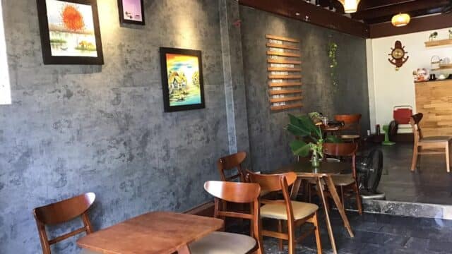 A cozy cafe with wooden tables, chairs, wall art, and plants against a gray textured wall.