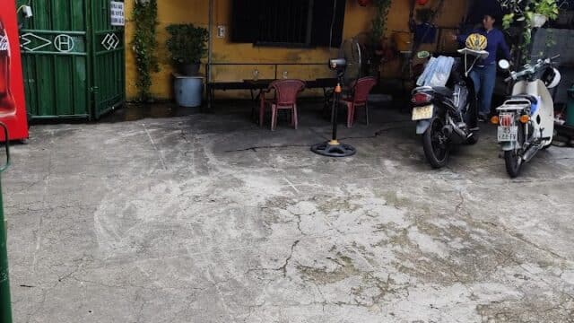 Two people near motorcycles outside a yellow Hoi An building with red lanterns and a green gate.