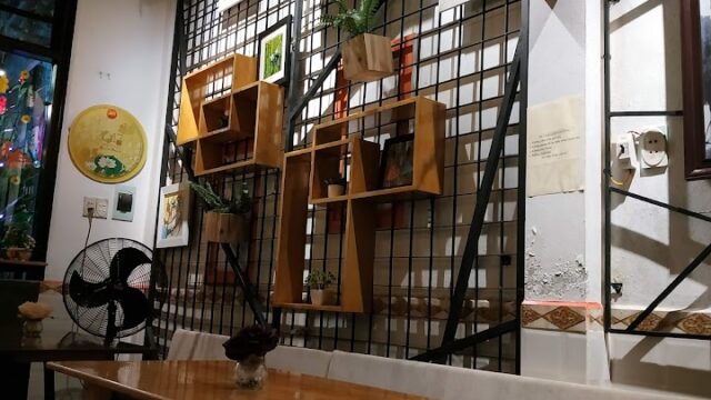 Wooden table and bench in a cozy Hoi An café with wall-mounted shelves, plants, and framed art on a grid wall.