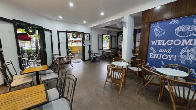 A cozy Hoi An café with wooden tables and chairs, bright lighting, and a Welcome and Enjoy sign on the wall.