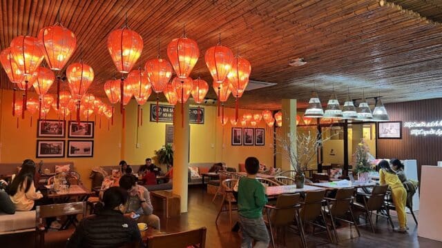 A cozy Hoi An restaurant with red lanterns, wooden decor, and people dining and talking at tables.
