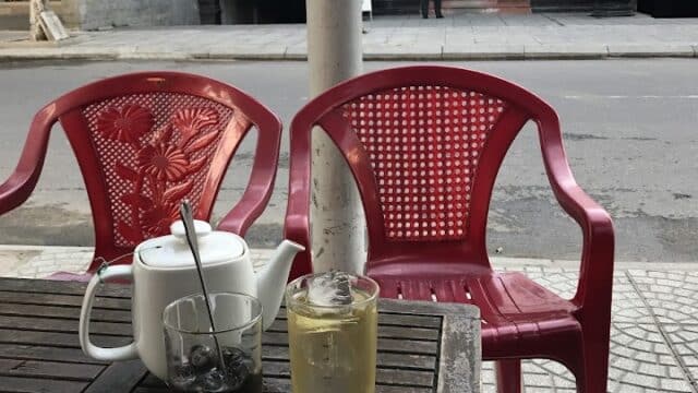 Iced drinks and a teapot on a table with red chairs capture the laid-back vibe of Hoi An’s charming streetside cafés.