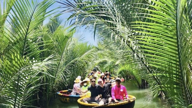Tourists with Captain Chris paddle round boats through a lush, green waterway lined with tall palms under a blue sky.