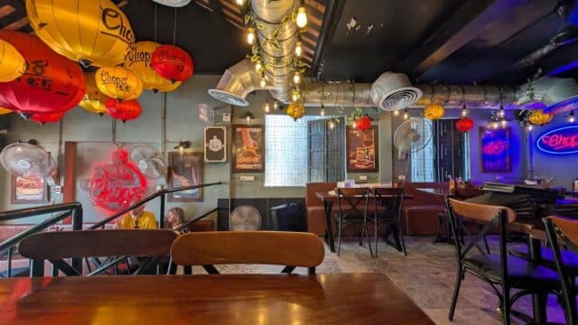 A cozy Hoi An restaurant interior with colorful lanterns, wooden tables, neon signs, and wall art on display.
