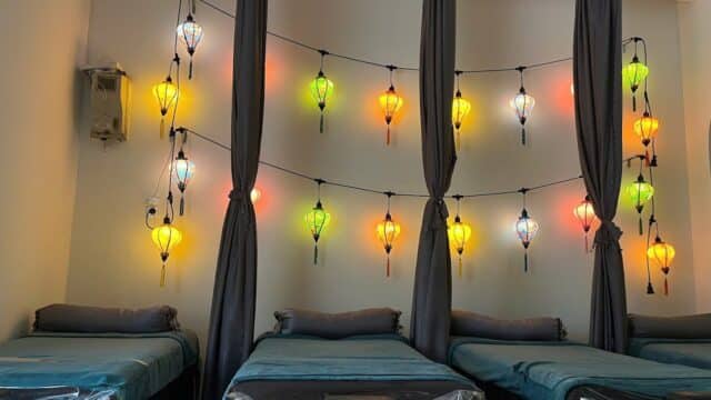 Three spa beds with teal linens and colorful lanterns hanging on the wall above them.