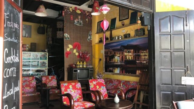 A cozy cafe with floral chairs, a round table, lanterns, and a blackboard menu by the entrance.