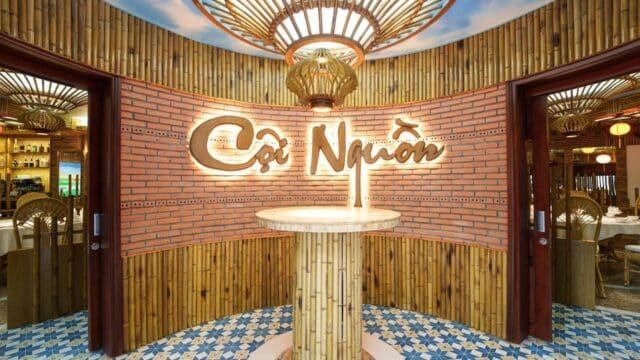 Bamboo and brick restaurant entrance in Hoi An with a round bamboo table and “Cội Nguồn” sign on the wall.