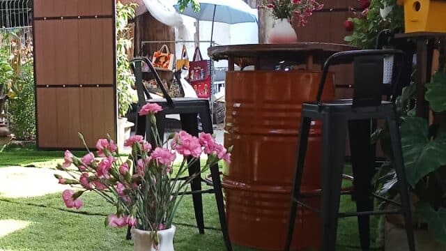 Outdoor cafe with a metal table, pink flowers, and a Cơm Gà Bà Hạnh sign in the background.
