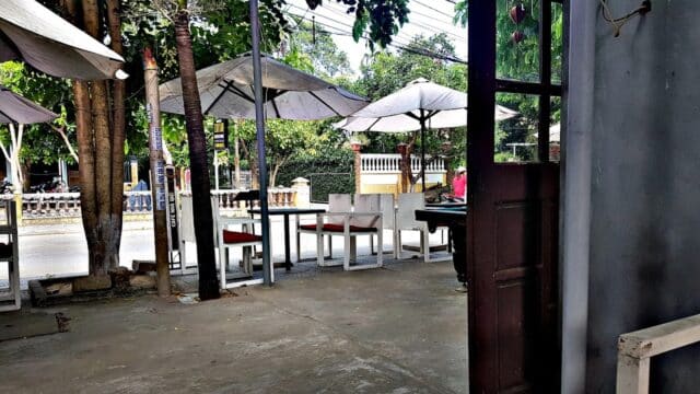 Outdoor cafe seating at Country House Coffee, with tables, chairs, and umbrellas near a street, viewed from a shaded entrance.