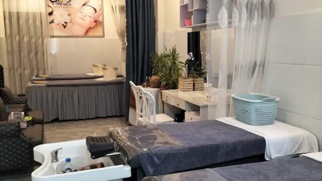 Two salon beds with hair wash sinks in a modern, well-lit beauty spa with relaxing decor and a facial poster.