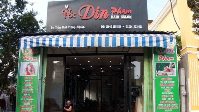 Front view of Din Pham beauty salon with striped awning, glass doors, and green service signs on both sides.