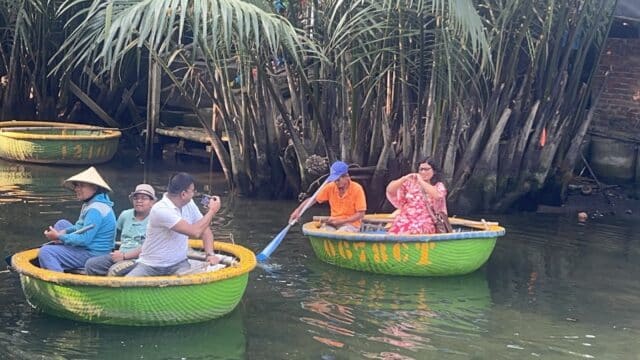 People enjoy a Basket Boat Tour, riding round basket boats on a river lined with palm trees, taking photos and soaking in the scenery.