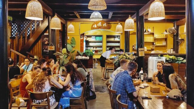 People dining and chatting in Everyday Restaurant, a cozy spot with wooden decor and warmly glowing hanging lamps.