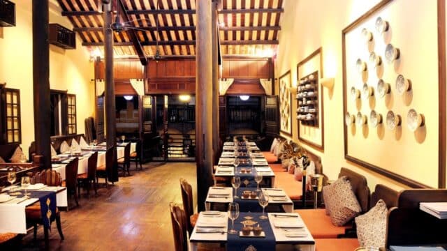Elegant restaurant interior with wooden beams, neatly set tables, cushioned bench seating, and decorative wall plates.