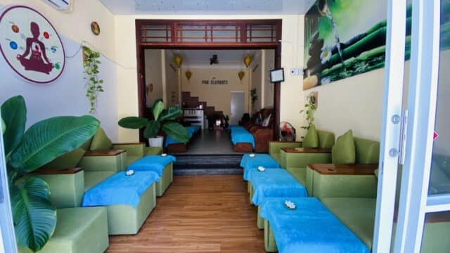 The Five Elements Spa waiting area features green seats, blue towels, lush plants, and a calm, inviting atmosphere.
