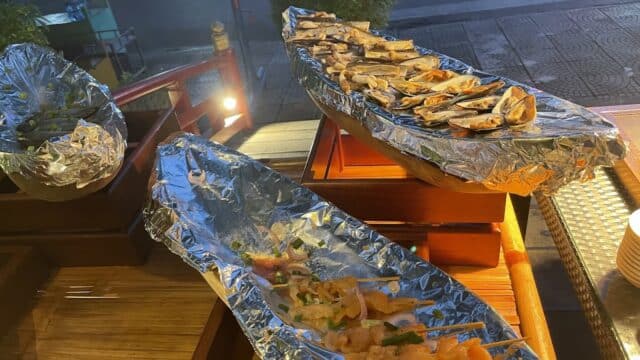 Seafood skewers and mussels on foil trays at a vibrant Hoi An outdoor food stall in the evening.