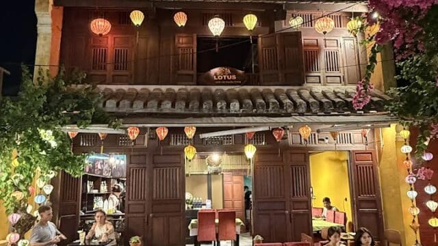 Two-story café at night with lotus lanterns, wooden shutters, and people dining outdoors under vibrant lighting.