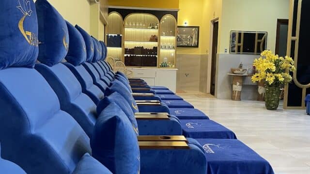 Row of plush blue recliner chairs in Gecko Beauty Salon's spa lounge, with yellow walls and lush indoor plants visible.